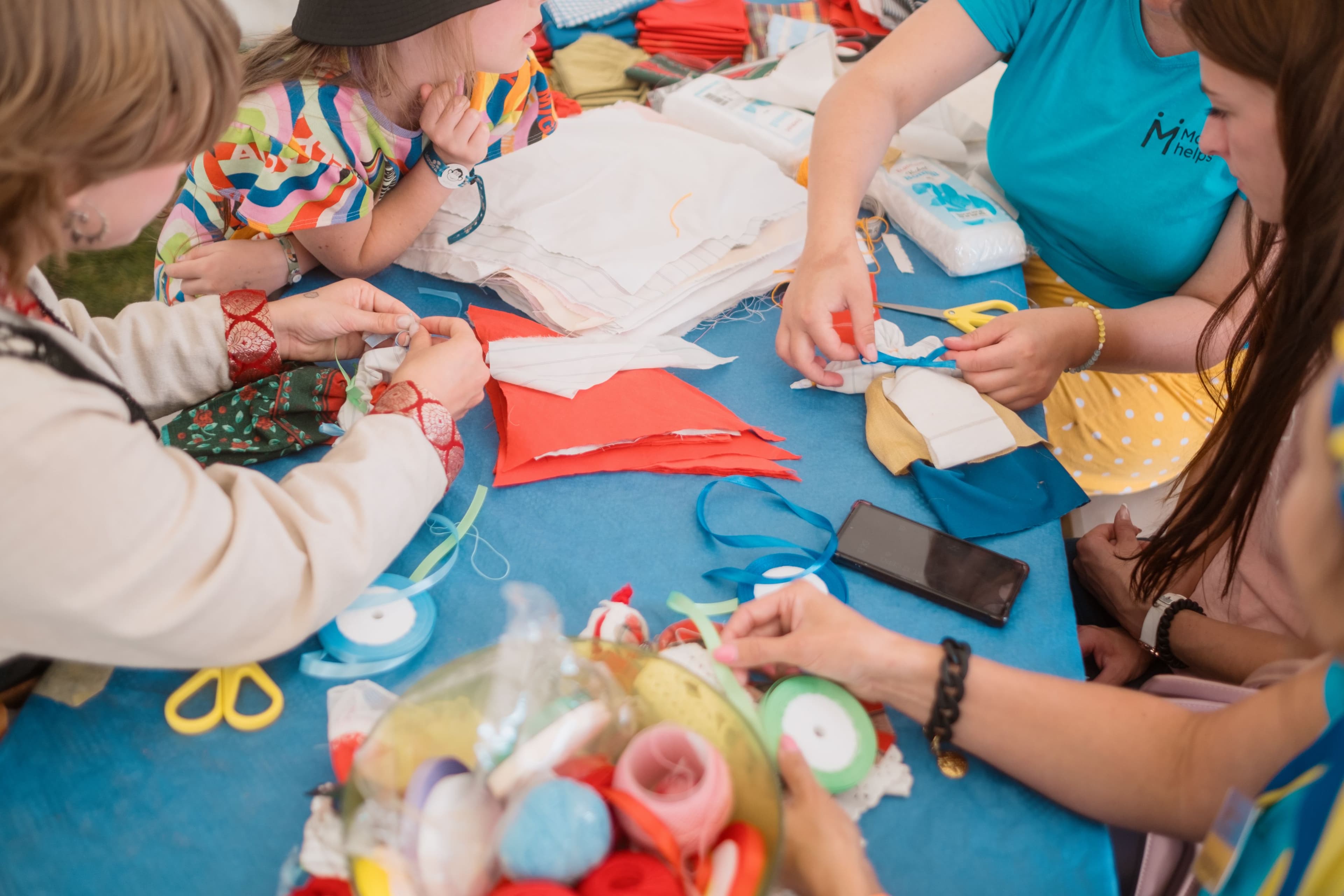 Barn och vuxna pysslar med tyg, band och saxar vid ett bord under en workshop på Malmöfestivalen.