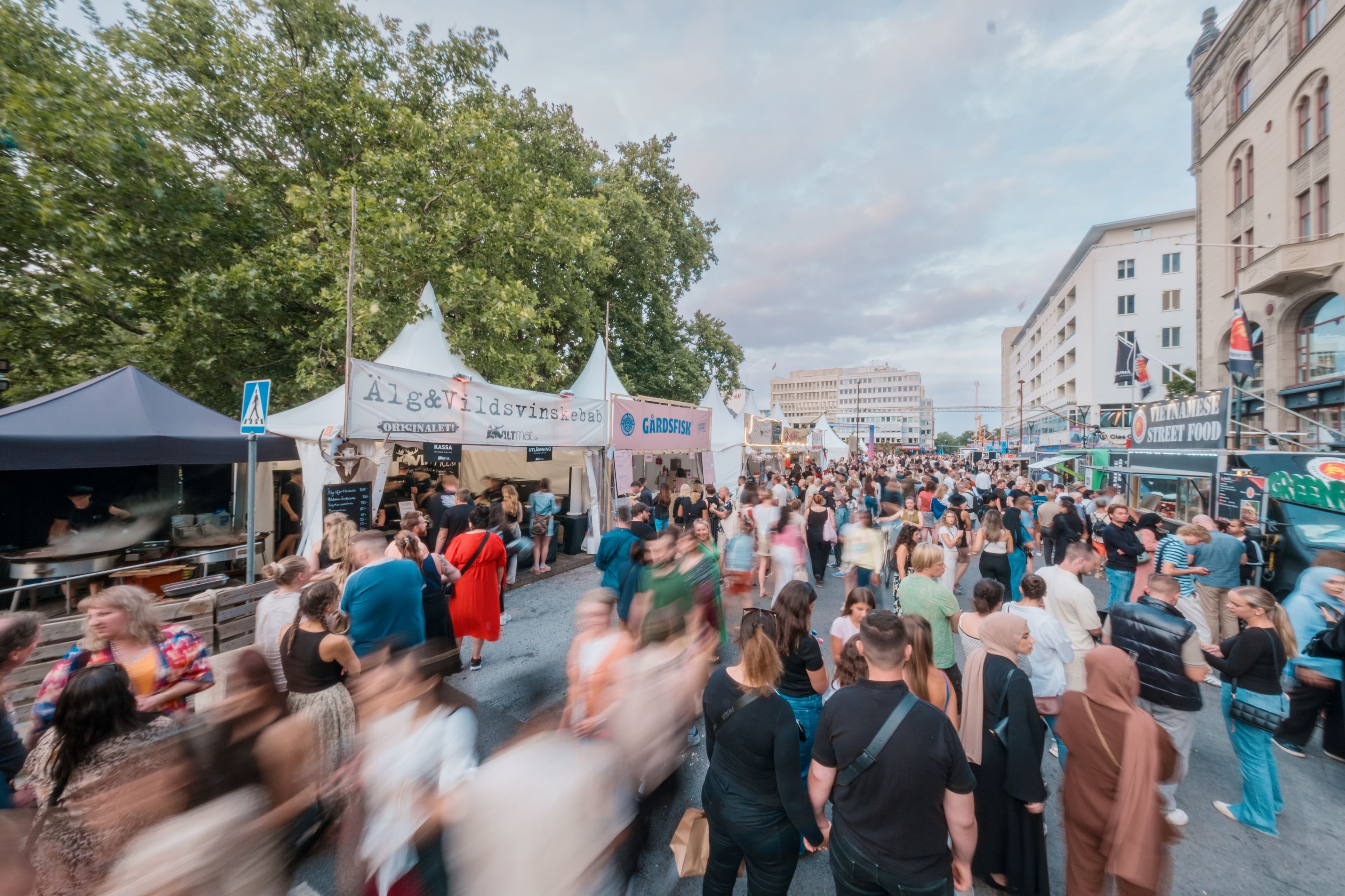 Människor promenerar längs en matgata med mattält och food trucks under Malmöfestivalen.